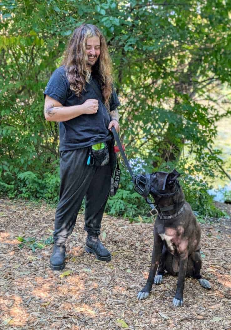 man standing next to black dog with treat in hand